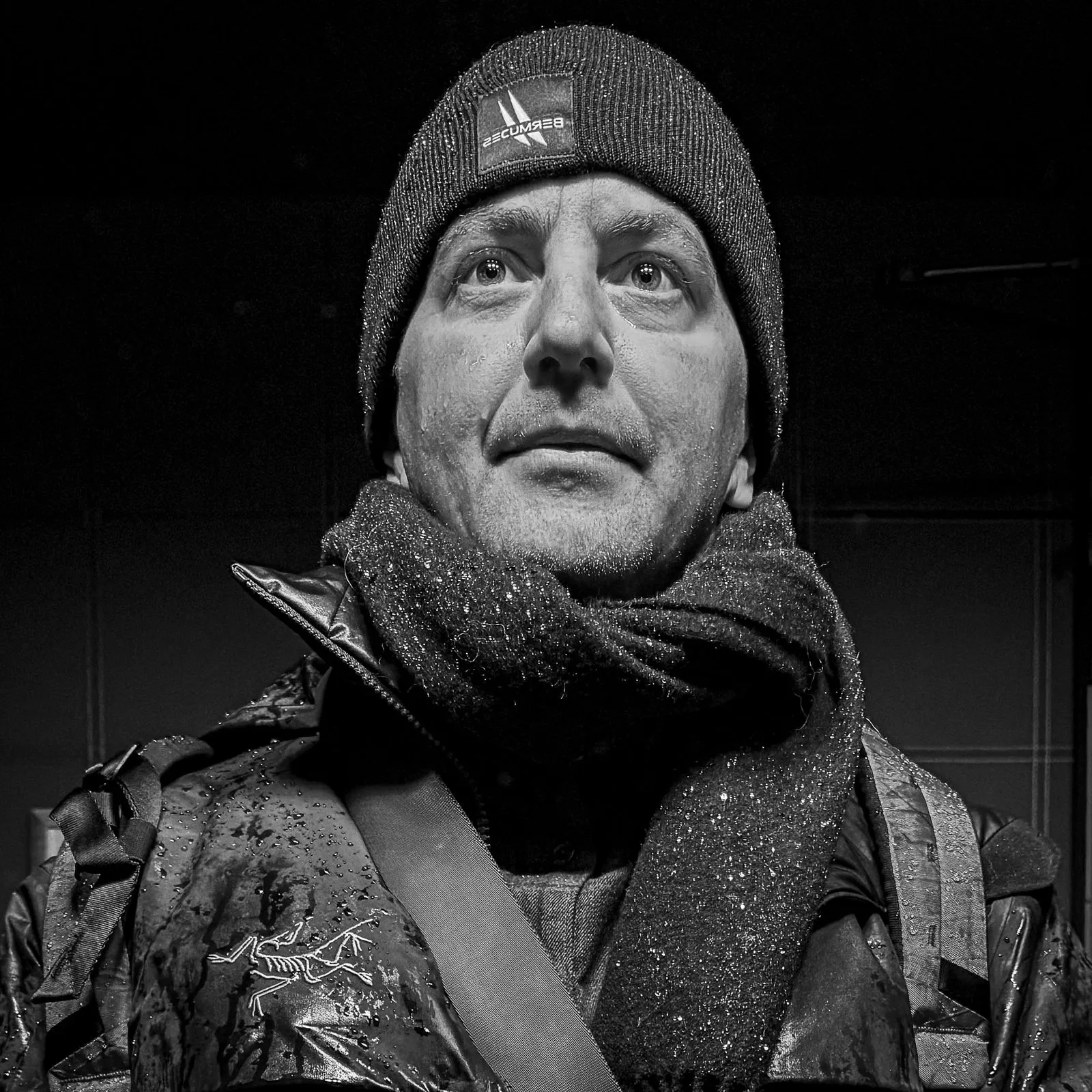Edward in a knit cap and scarf, rain on the jacket, looking up into the light.